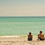 Couple sitting on the sand with the ocean in the background on a hot sunny day